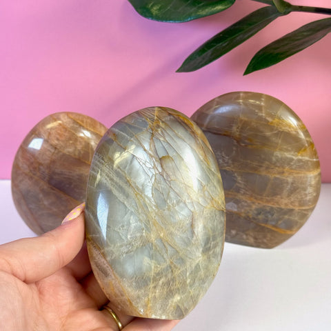Polished peach moonstone free form crystal with natural striations, held in hand.