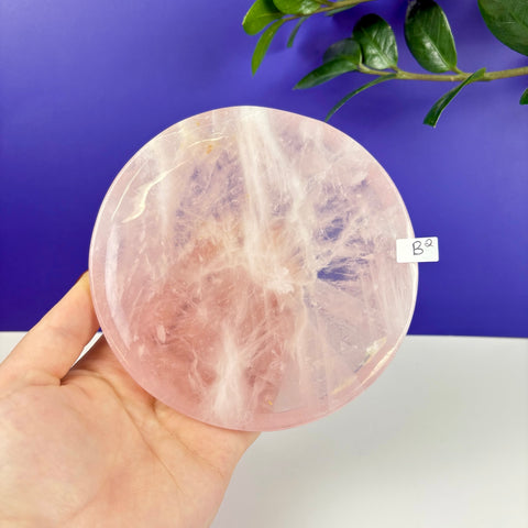 Round rose quartz crystal plate with natural veining held in a hand against a purple background.