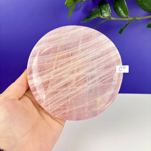 Handheld circular rose quartz plate with natural white veining and a polished finish against a blue background.
