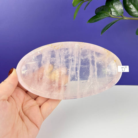 Handheld oval-shaped rose quartz crystal plate with translucent pink hues and natural internal veining.