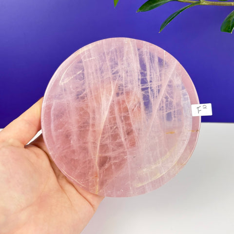 Handheld circular rose quartz plate with natural pink crystalline textures and a polished finish.