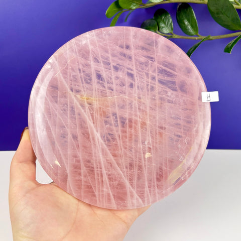 Handheld circular plate made of translucent, pale pink rose quartz with natural crystalline veining.