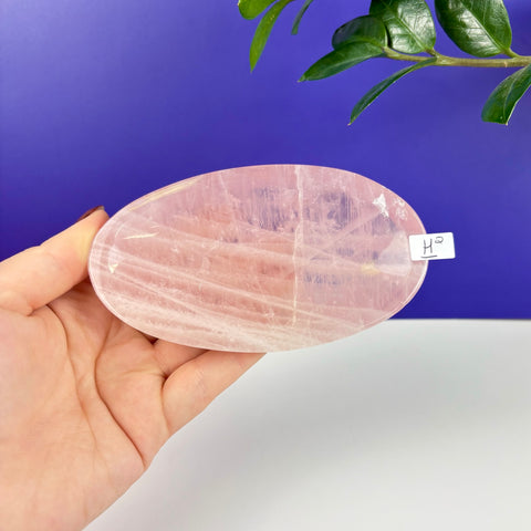 Handheld oval-shaped rose quartz crystal plate with natural translucent pink veining and a smooth polished finish.