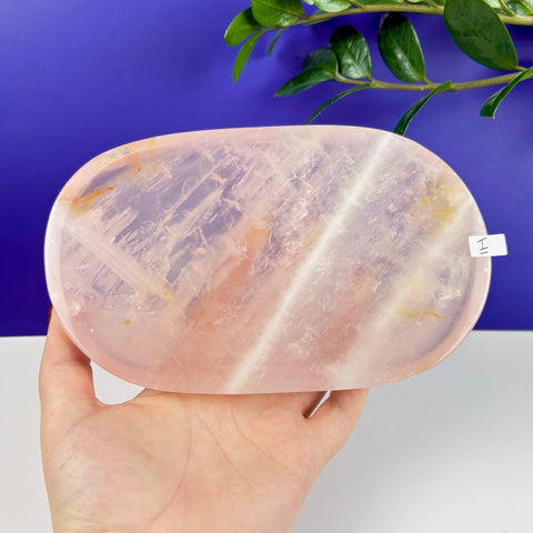 Hand held oval rose quartz crystal plate with natural translucent pink tones and unique mineral inclusions.