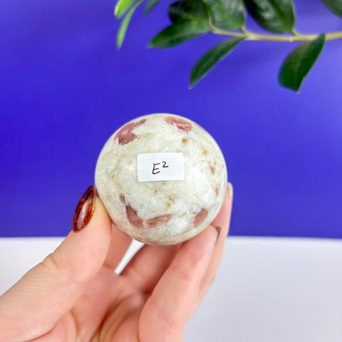 Polished pink tourmaline sphere with white quartz matrix held in a hand against a blue background.