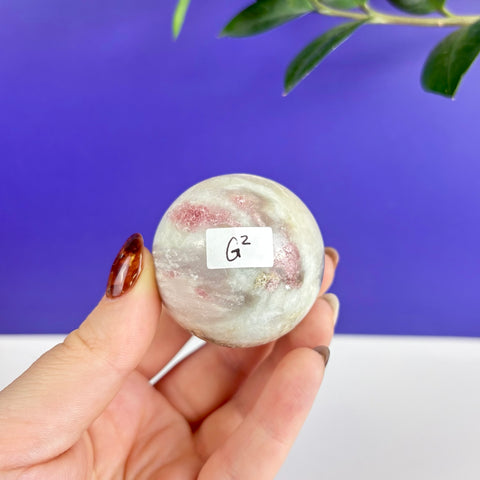 Polished pink tourmaline crystal sphere with white inclusions held in hand against a blue background.