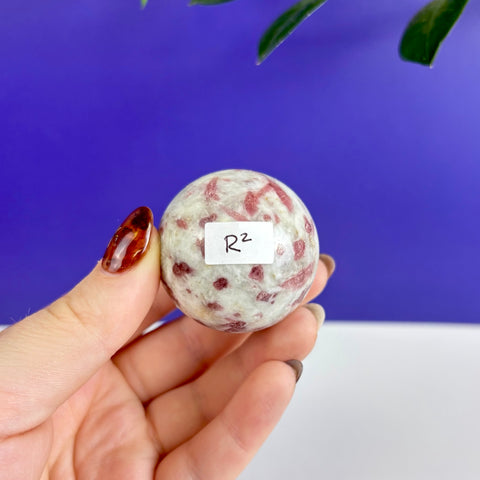 Polished pink tourmaline sphere with white matrix held in hand against a blue background.