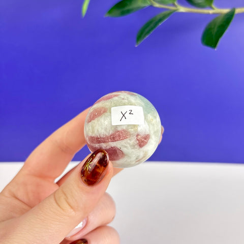 Polished pink tourmaline sphere with white mineral inclusions held in a hand against a blue background.