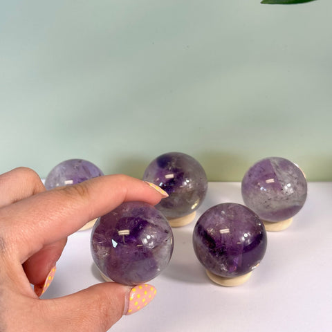 Hand holding a deep purple Phantom Amethyst Sphere, with four more spheres on wooden stands.