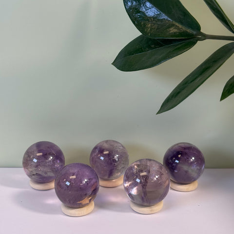 Five polished phantom amethyst spheres with purple inclusions, resting on light wooden stands.