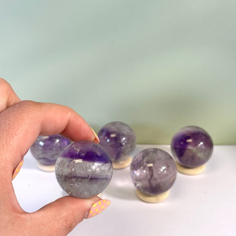 Hand holding a clear and purple phantom amethyst sphere, with four more spheres on stands in the background.