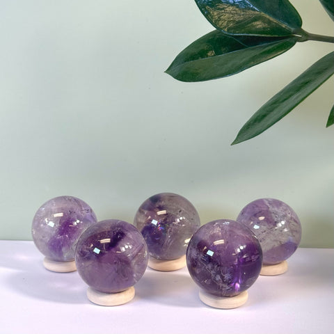 Five polished Phantom Amethyst spheres, deep purple with white inclusions, on light wooden stands.