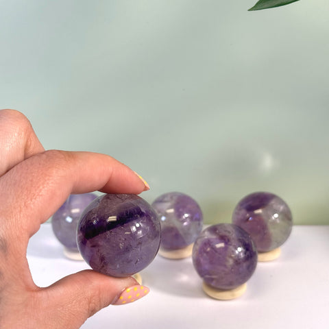 Hand holding a small, polished purple phantom amethyst sphere with several more in the background.