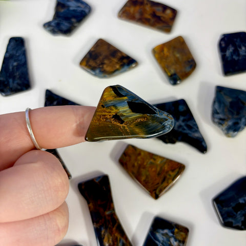 Polished triangular Pietersite slice with swirling blue and gold chatoyant patterns held against a white background.