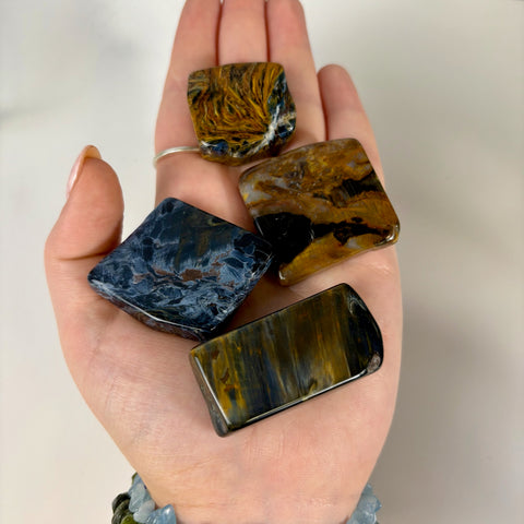 Four polished Pietersite slices with swirling blue and golden-brown chatoyant patterns held in a palm.