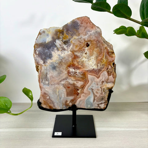 Large pink amethyst slab with agate banding and crystalline textures on a black metal display stand.