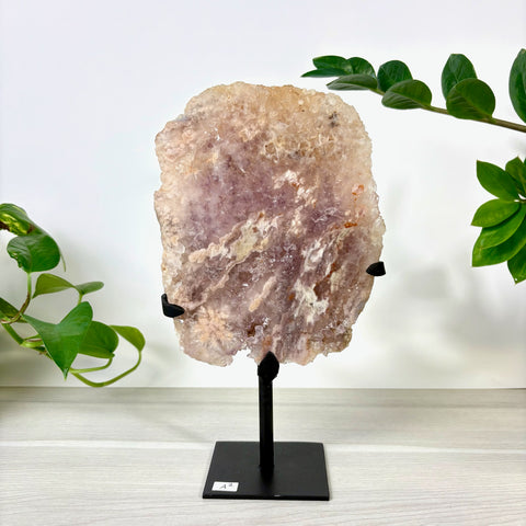 Rough-cut pink amethyst slab with crystalline texture on a black metal display stand against a white background.