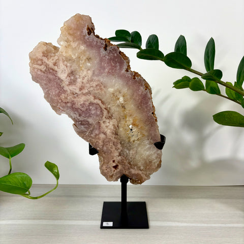 Large pink amethyst crystal slab with white quartz center, displayed on a black metal stand against a white background.