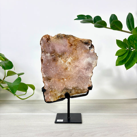 Large pink amethyst crystal slab with natural crystalline texture displayed on a black metal stand.