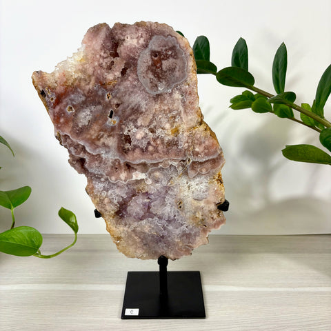 Large pink amethyst crystal slab with sparkling druzy geode center, displayed on a black metal stand.