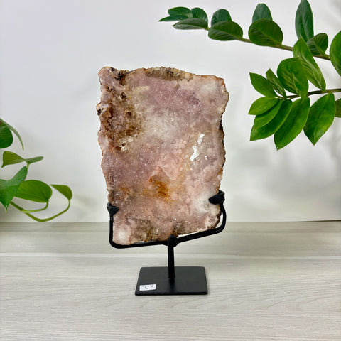 Large pink amethyst crystal slab on a black metal display stand, featuring natural crystalline textures and earthy edges.