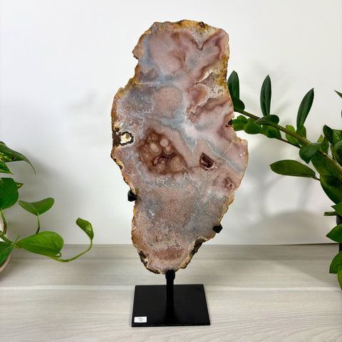 Large pink amethyst slab with crystalline textures and natural edges, displayed on a black metal stand.