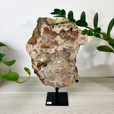Large pink amethyst geode slice with crystalline textures on a black metal display stand.