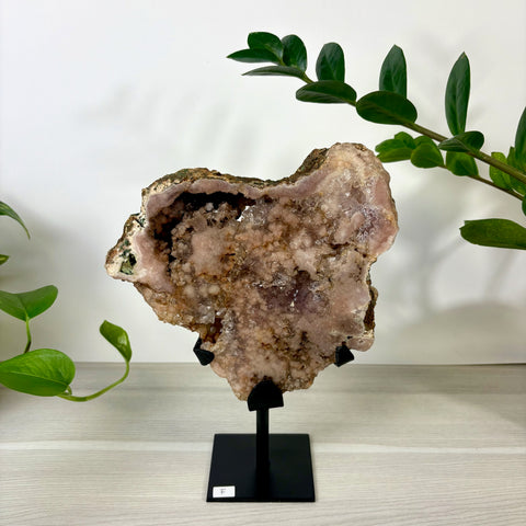 Large pink amethyst geode cluster with sparkling crystals on a black metal display stand against a white background.
