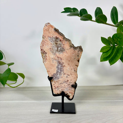Pink amethyst crystal slab with white quartz geode center, displayed on a black metal stand against a white background.