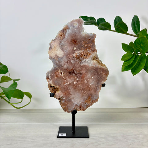 Large pink amethyst crystal slab with natural textured surface on a black metal display stand.
