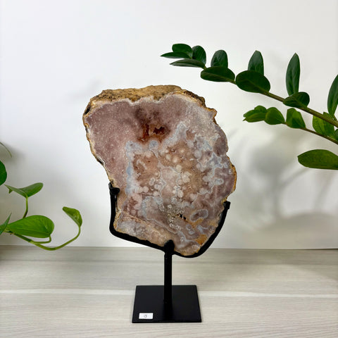 Large pink amethyst geode slice with white crystalline patterns displayed on a black metal stand.