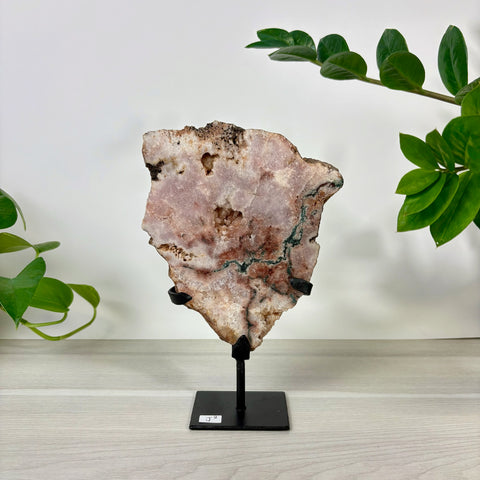 Pink amethyst crystal slab with natural mineral inclusions, displayed on a black metal stand against a white background.