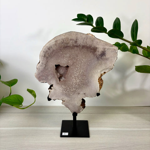 Large pink amethyst crystal slab with a central geode cavity, displayed on a black metal stand on a wooden surface.
