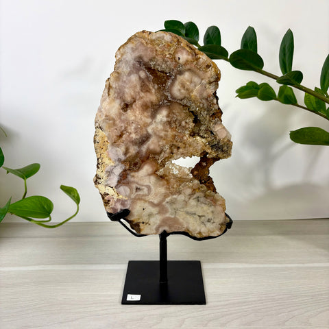 Large pink amethyst geode slab with crystalline textures on a black metal display stand.