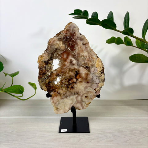 Pink amethyst crystal slab with natural hollow cavities, displayed on a black metal stand against a white background.