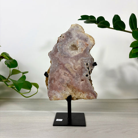 Large pink amethyst geode slice with a central crystal cavity, displayed on a black metal stand.