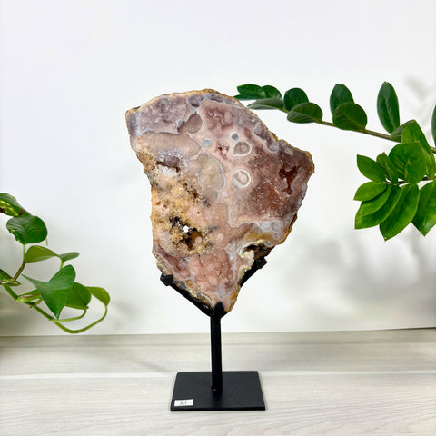 Large pink amethyst geode slice with crystalline textures on a black metal display stand.
