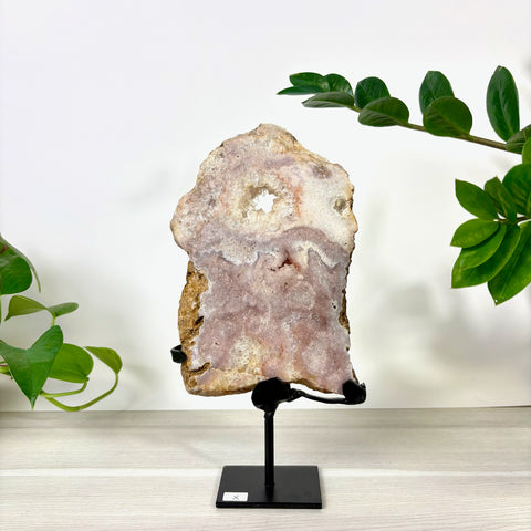 Pink amethyst crystal slab with a central geode opening, displayed on a black metal stand against a white background.