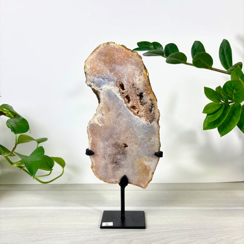 Pink amethyst crystal slab with natural geode center on a black metal display stand against a white background.