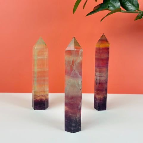 Three polished Poison Candy fluorite crystal towers featuring vibrant bands of purple, yellow, and clear mineral inclusions.