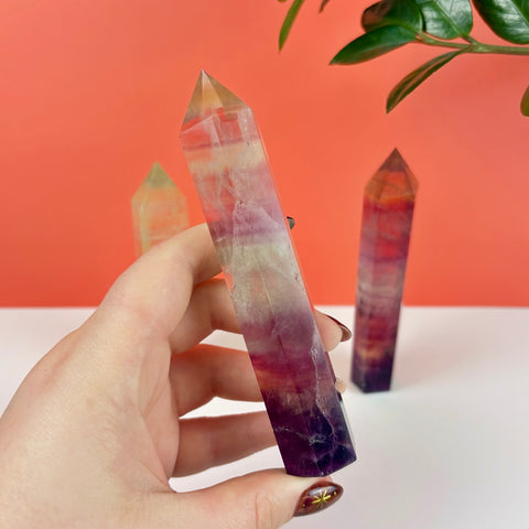 Hand holding a polished Poison Candy fluorite crystal tower with vibrant purple, pink, and clear banded layers.