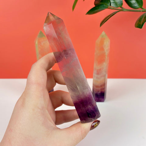 Handheld Poison Candy fluorite crystal tower featuring translucent purple, yellow, and clear banded mineral layers.