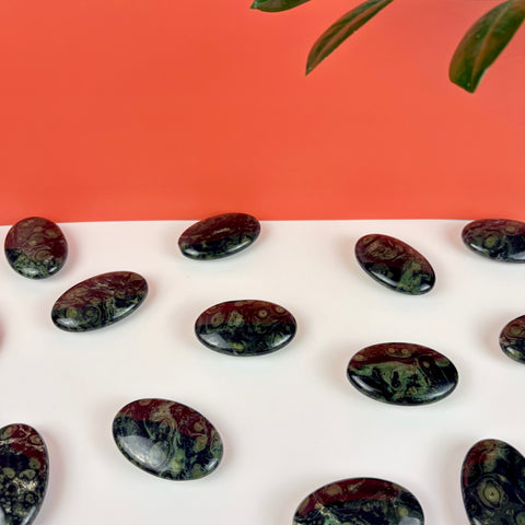 Polished Kambaba Jasper palm stones with dark green and black orbicular patterns arranged on a white surface.