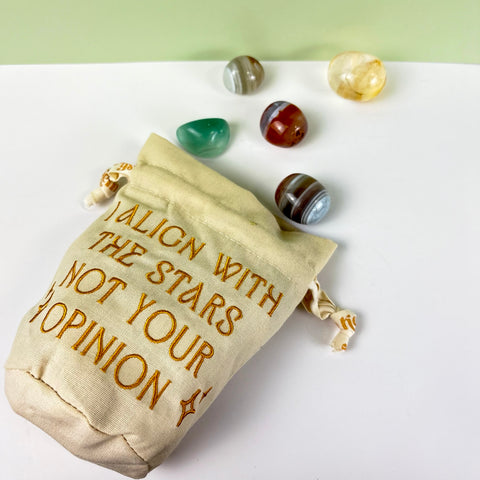 Cream canvas drawstring pouch with gold embroidery and polished crystals on a white surface.