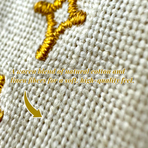 Close-up of cream-colored cotton and linen canvas fabric with detailed gold embroidery.