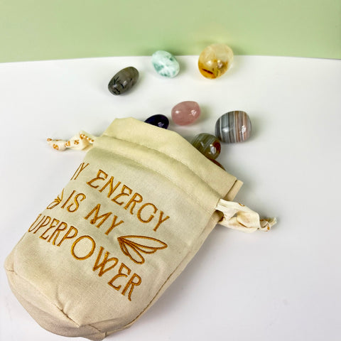 Cream cotton-linen drawstring pouch with gold embroidery and tumbled crystals spilling out.