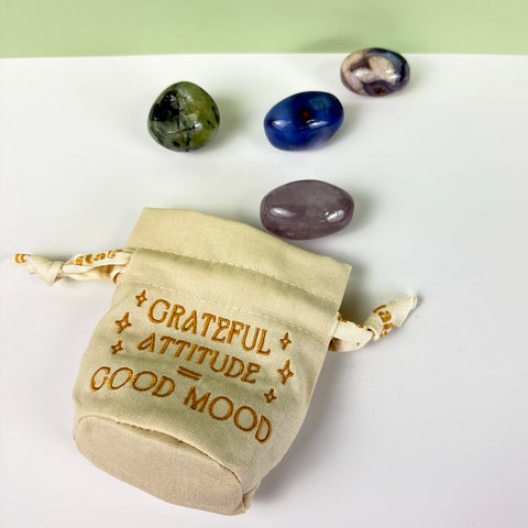 Small natural canvas drawstring pouch with gold embroidery and three polished crystals on a white surface.
