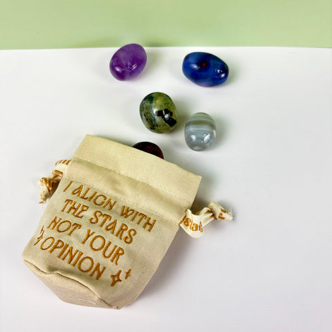 Small beige cotton-linen drawstring pouch with gold embroidery, featuring four polished crystals on a white surface.