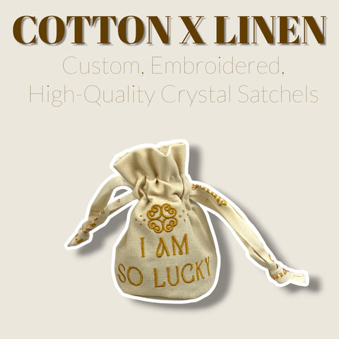 Small cream cotton-linen drawstring pouch with gold embroidered "I AM SO LUCKY" text and ribbon.