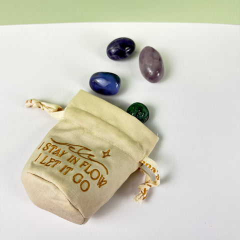 Small cream canvas drawstring pouch with gold embroidery and four tumbled crystals on a white surface.
